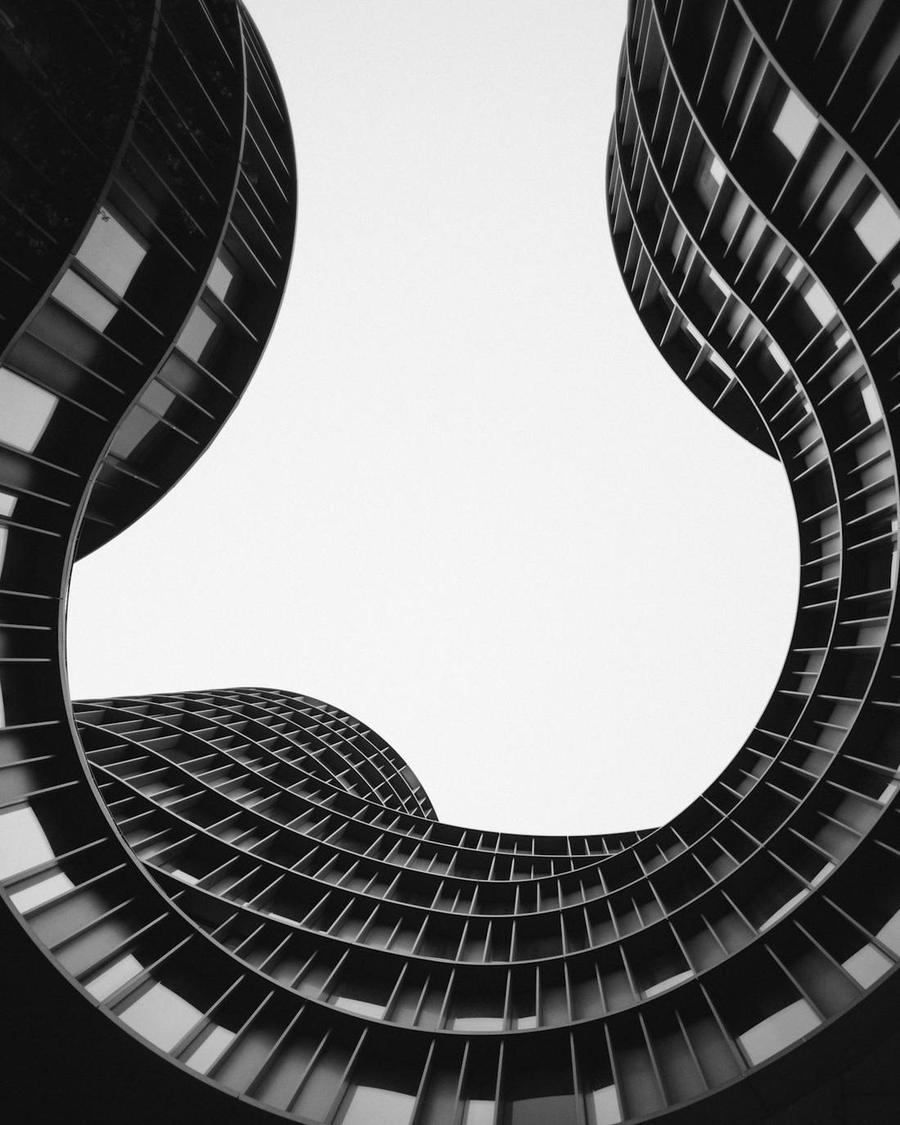 Looking upward between two curved high-rise facades toward open sky.